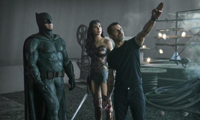 Zack Snyder puts his hand up and points in front of Batman and Wonder Woman.